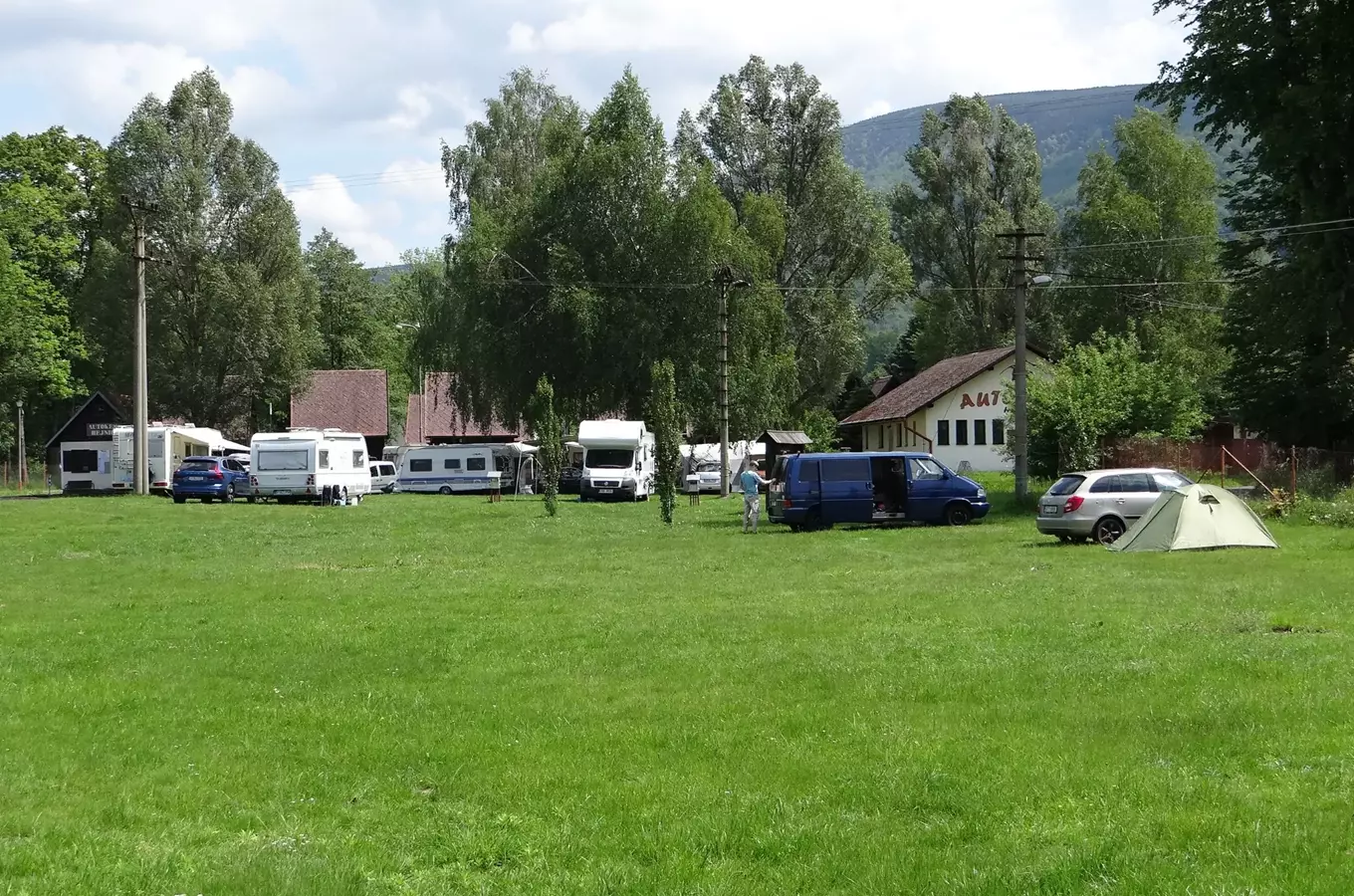 Autokemp v Hejnicích s karavanami, stany a vozy na trávníku.