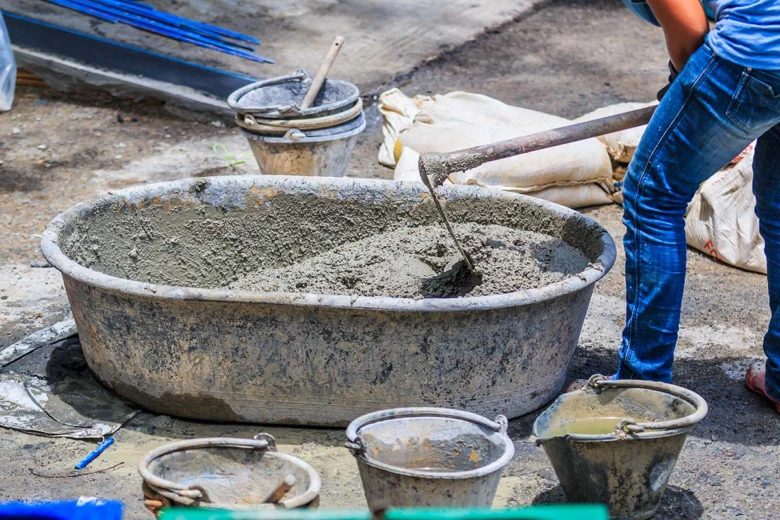 Pracovník míchá beton v velké nádobě na staveništi.