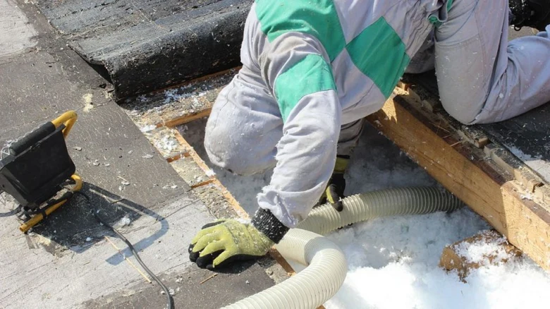 Pracovník fouká izolační materiál do střešního prostoru.
