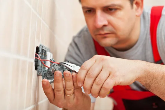 Elektrikář zapojuje dráty do elektrické zásuvky ve zdi.