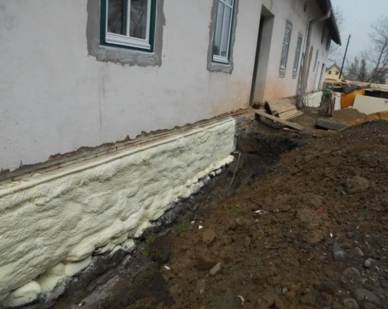 Bílá pěnová izolace na základové stěně domu proti vlhkosti.