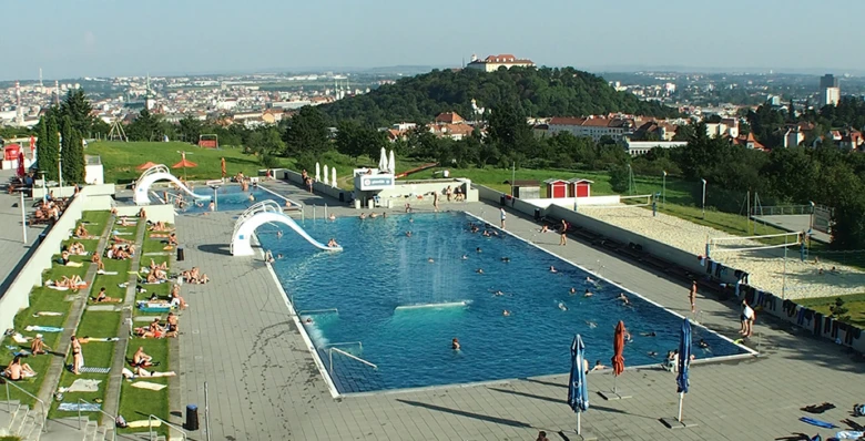 Venkovní bazén na kopci s tobogány a výhledem do města.