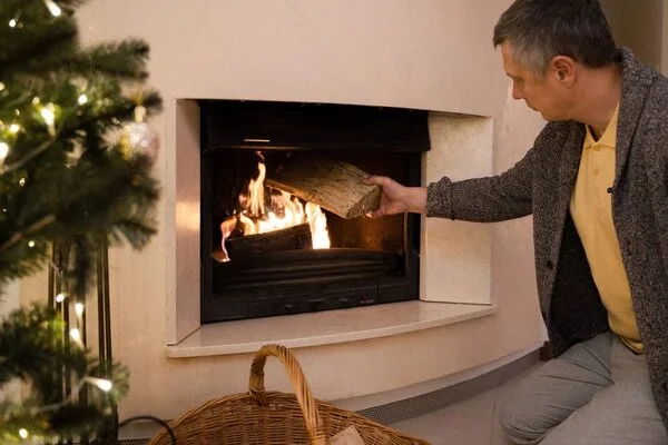 Muž vkládá dřevo do krbu v domácnosti.