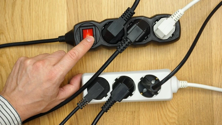 Ruka stiská tlačítko na elektrické zásuvce s více zapojenými kabely.