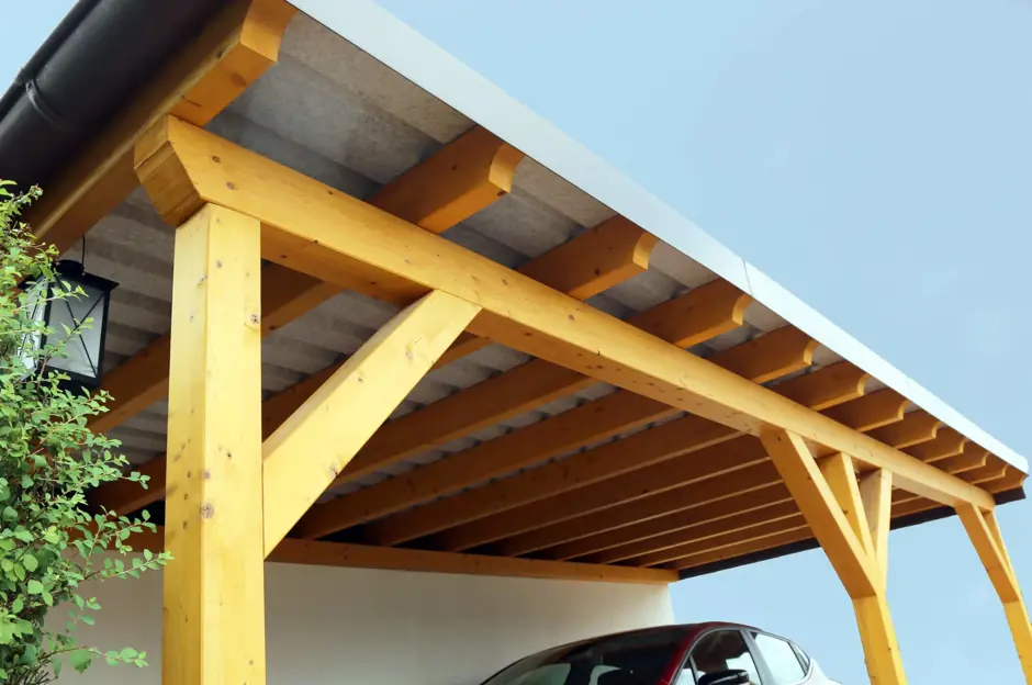 Nově postavený dřevěný přístřešek pro auto s žlutými trámy.