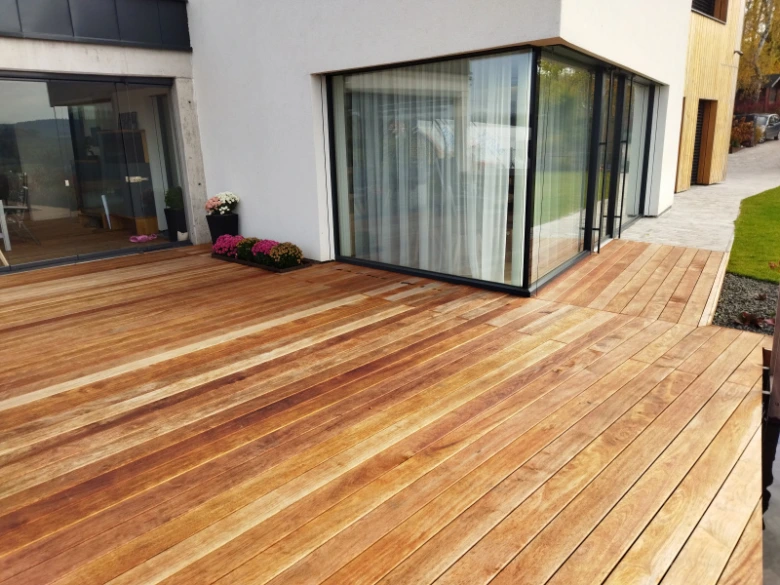 Moderní dřevěná terasa připojená k domu s velkými okny.