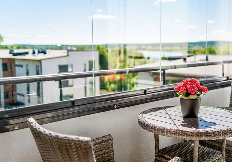 Moderní balkon s výhledem na vodu skrze zasklené panely.