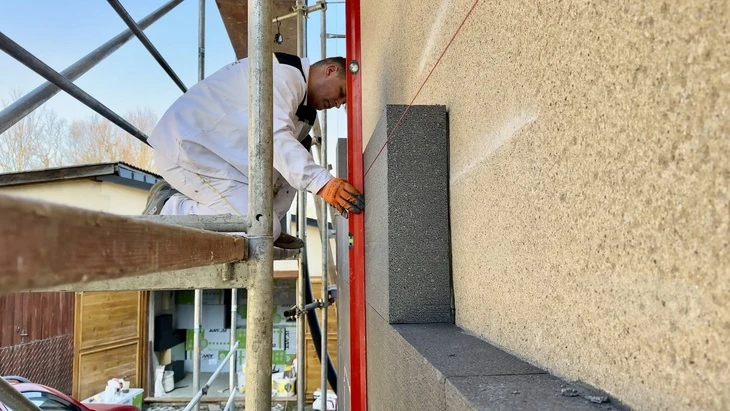 Stavebník lepi izolační desku na fasádu pomocí šablon.