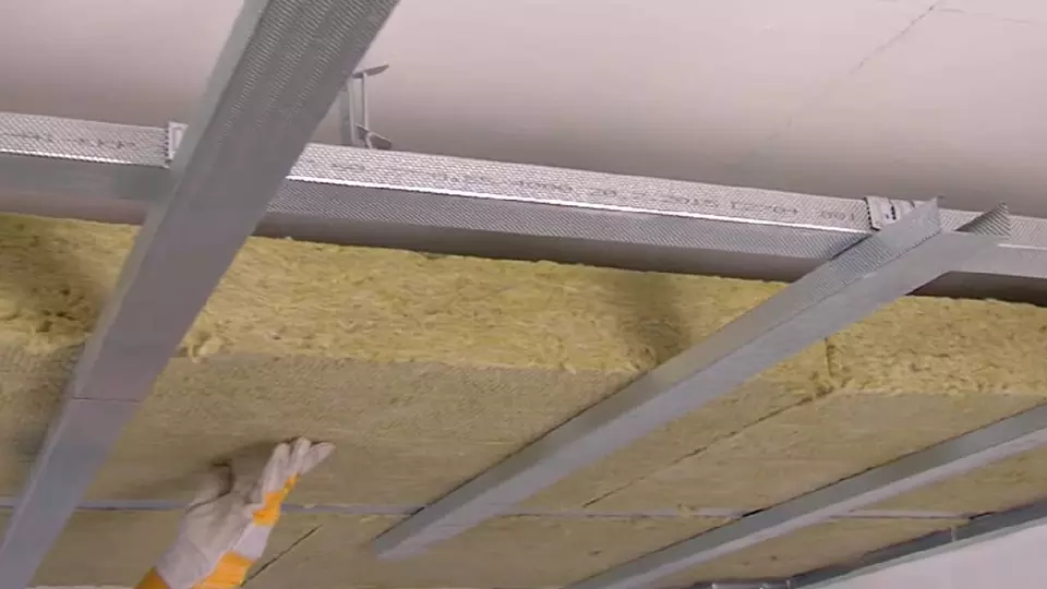 Ruční instalace žluté izolační vaty mezi ocelovými nosníky.
