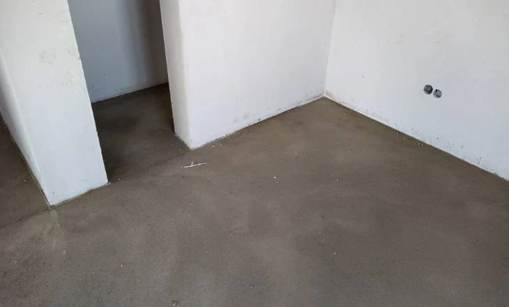 Nezhotovená betonová podlaha v interiéru s bílými stěnami.
