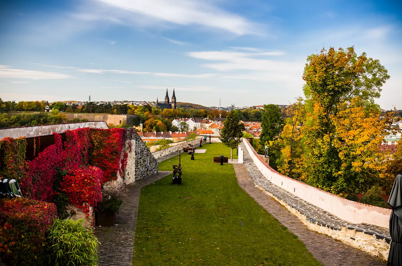 Zpevněná zahrada s výhledem na Prahu a historickou architekturu.