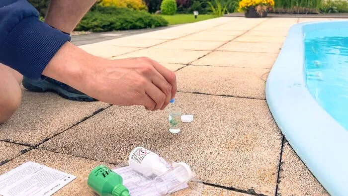 Ruka drží chemii pro kontrolu vody v bazénu vedle plaveckého bazénu.