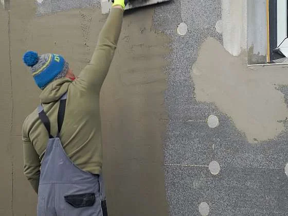 Stavebník nanáší lepidlo s perlinkou na fasádu.