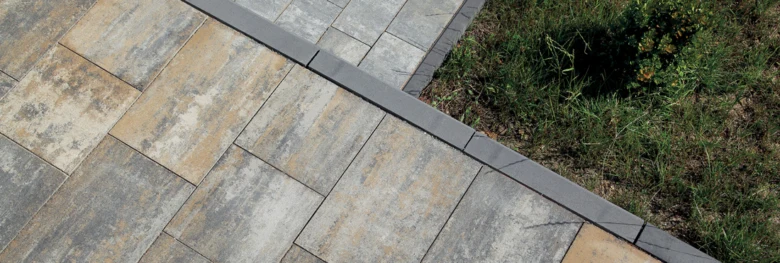 Pohled na dlažbu s obrubníkem z betonu vedle trávníku.