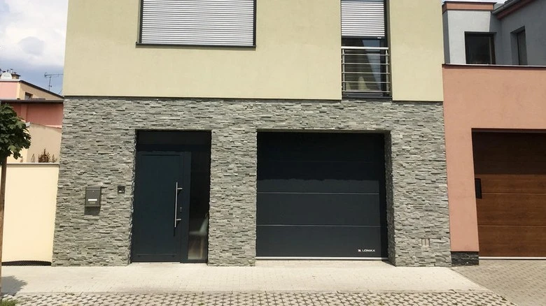 Moderná garážová brána vedle vchodu do domu s kamennou fasádou.