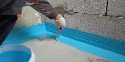 Práce na hydroizolaci koupelny: aplikace modré těsnicí hmoty štětcem.