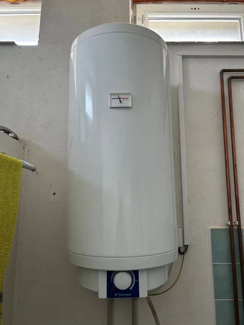 Bílý elektrický bojler na zdi s teploměrem a ovládacím panelem.