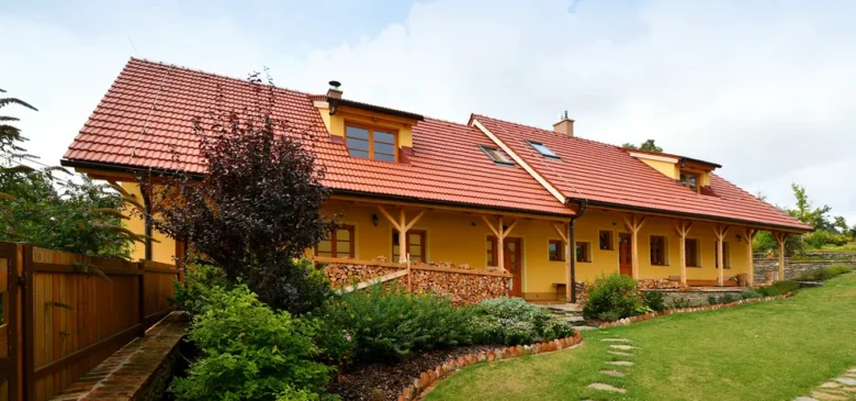 Žlutý dům s keramickou červenohnědou střešní krytinou.