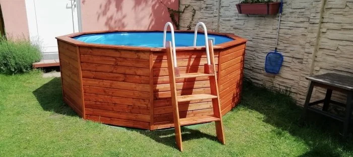 Nadzemní bazén obložený dřevem s žebříkem na trávníku.