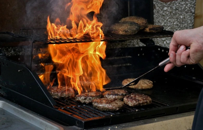 Grilování hamburgerů na zahradním krbu s plameny