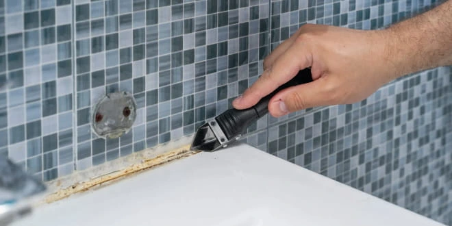 Ruční odstraňování starého silikonu kolem vany před aplikací nového.