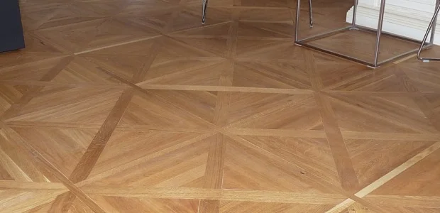 Pohled na dřevěnou parketovou podlahu s geometrickým vzorem hvězdicového tvaru.