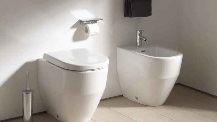 Moderní koupelna s bílým záchodem vedle umývadla pro hygienu.