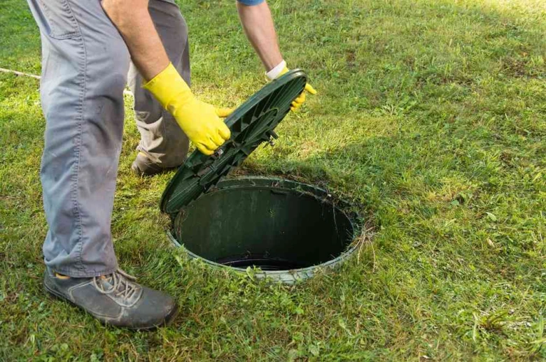 Pracovník otevírá poklop septiku na trávníku.