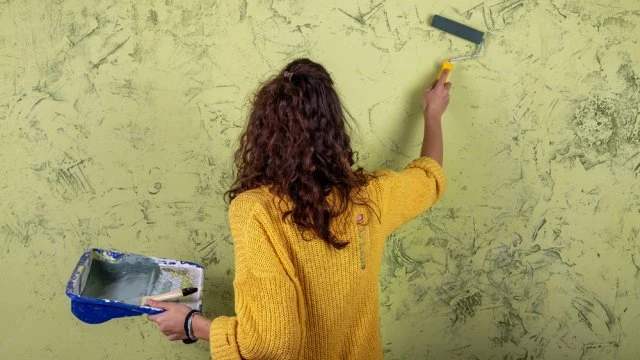 Žena malířka aplikuje texturu na zeď válečkem.