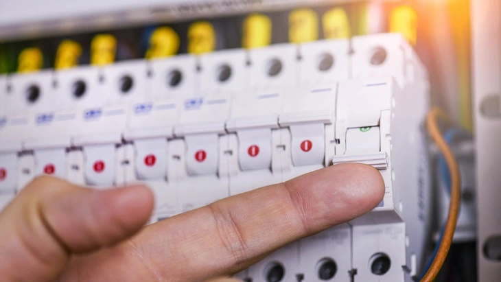 Ruka zapíná jistič v domovním rozvaděči pro elektroinstalaci.