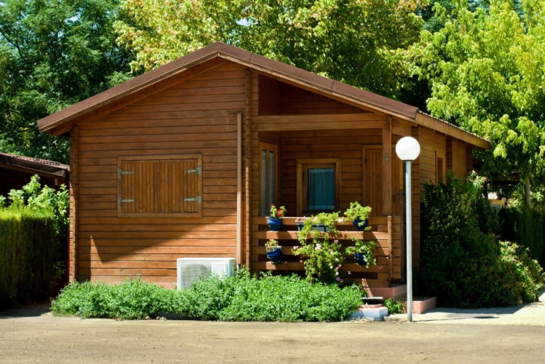Dřevěný zahradní domek s okny, balkónem a okolním zelením.