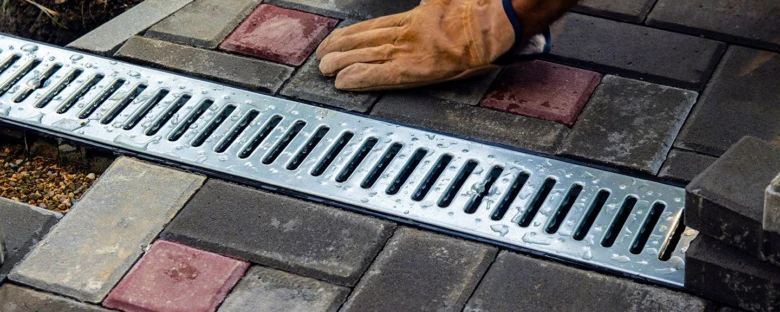 Instalace odtokového žlabu mezi dlažebními kostkami v zahradě.