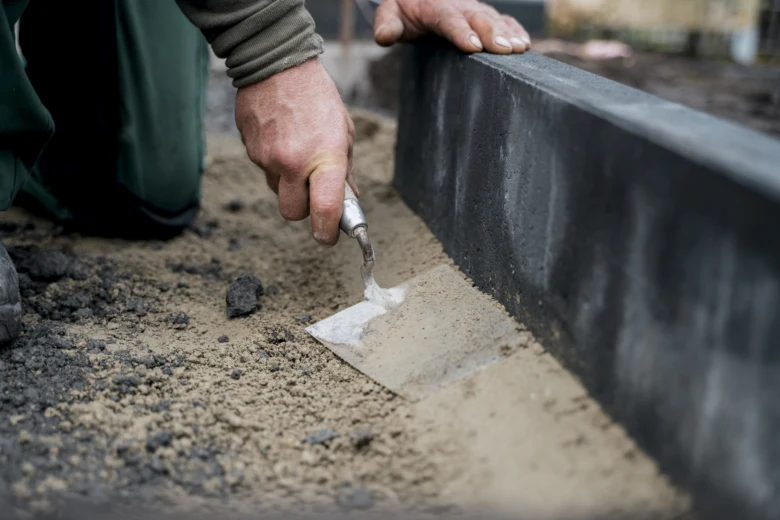 Muž hladí beton u obrubníku špachtlou.
