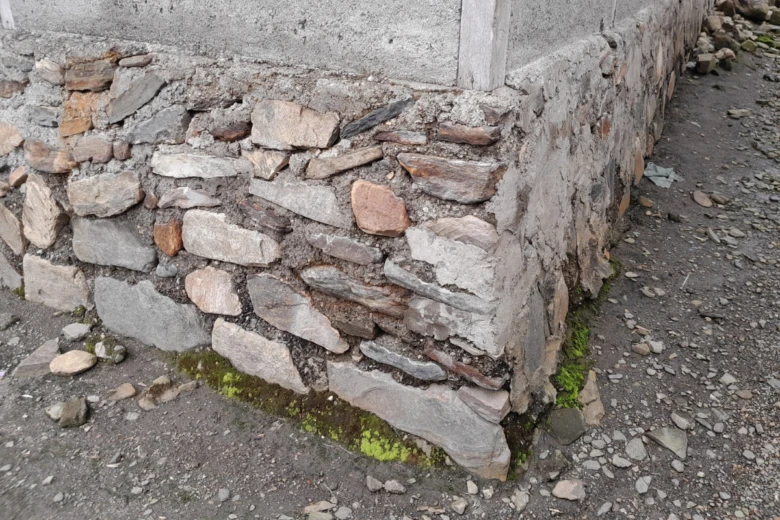 Hrubý kamenný základ starého domu s rohem z betonu.