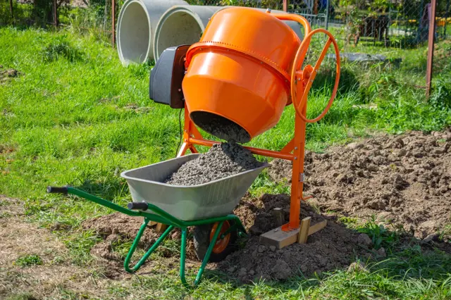 Oranžová betonova míchačka nalévá směs do vozíku na trávníku.