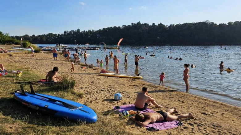 Lidé plavou na břehu jezera v Praze za slunečného dne.