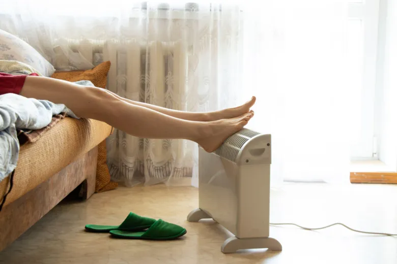 Osoba se vyhřívá na elektrickém radiátoru v domácnosti.