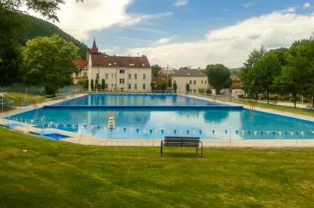 Venkovní bazén s travnatým okrajem a historickou budovou na pozadí.