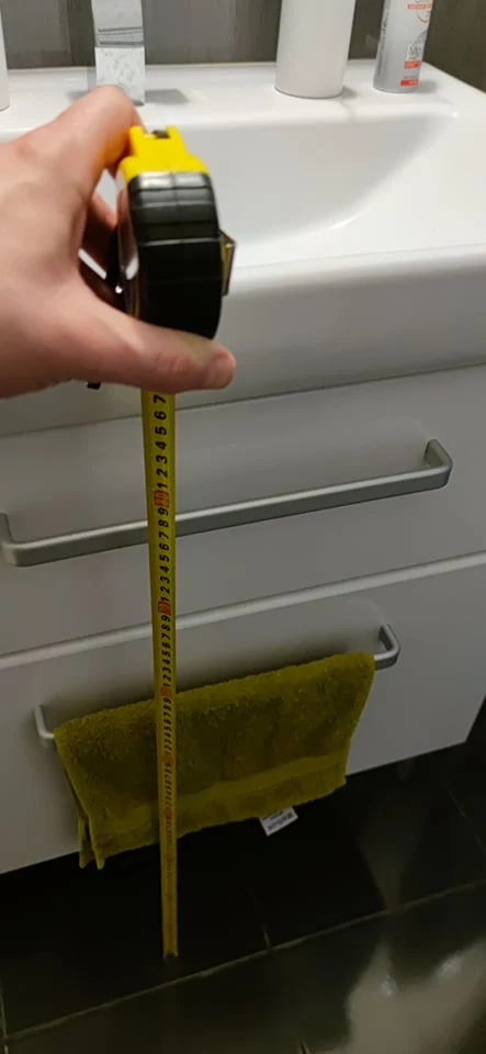 Ruční měření výšky umyvadla v koupelně páskou.