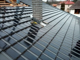 Fotovoltaické střešní tašky na tmavé střechě s komínem.