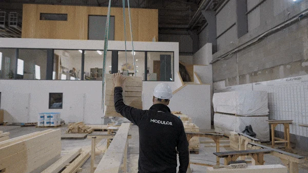 Stavebník zvedá modulární dřevěné stěny v továrně.