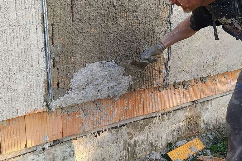 Stavebník nanáší omítku na cihlovou zeď pomocí stěrky.