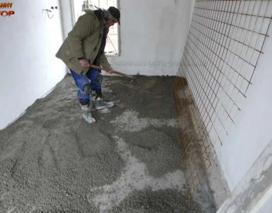 Muž nalévá betonovou podlahu s výztuhou pro topení.