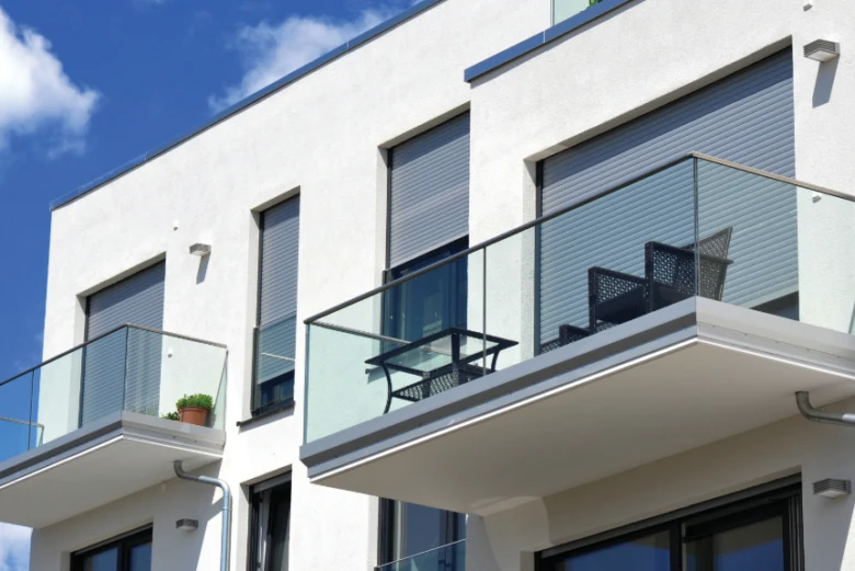 Moderní dům s venkovními roletami na balkónech pod modrou oblohou.