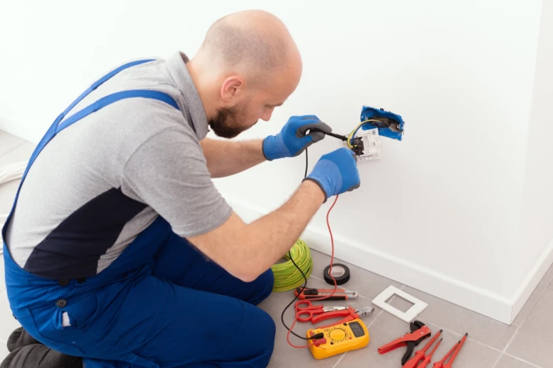 Elektrikář testuje dráty v zásuvce multimetrem při instalaci.