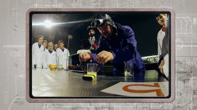 Muž ukazuje elektrický zkrat na stole před diváky.