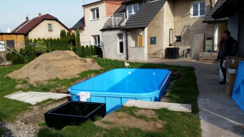 Modrý nadzemní bazén se instaluje v zahradě vedle domů.