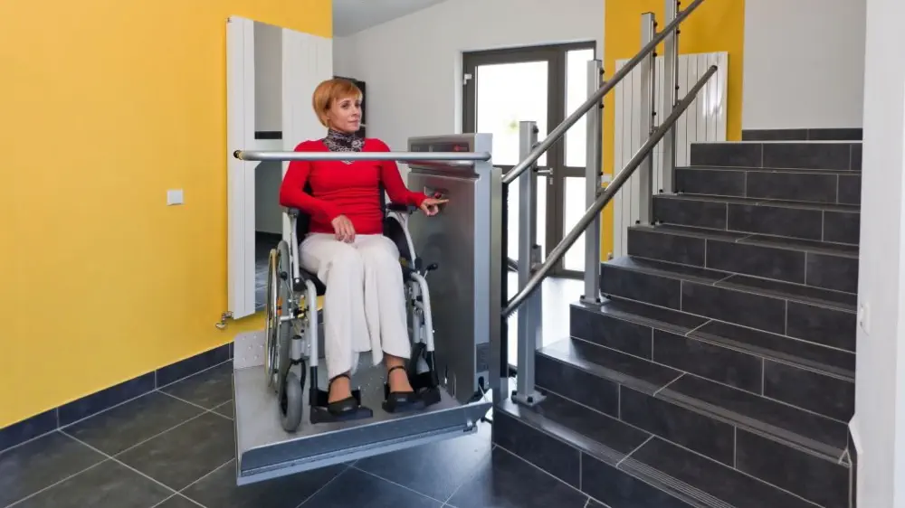 Žena v invalidním vozíku na schodišťové plošině uvnitř domu.