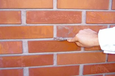 Ruka nanáší maltu mezi cihly při stavbě zdi.