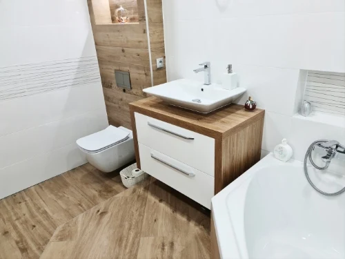 Moderní koupelna s dřevěným nábytkem a bílými sanitami.